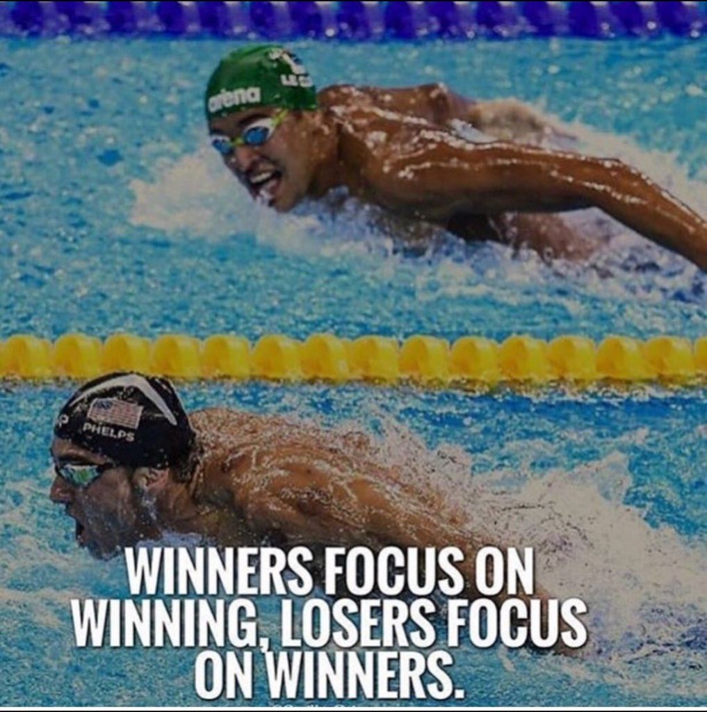 Two men swimming in a race. One is looking forward and the other is looking at him. Winners focus on winning, losers focus on winners.